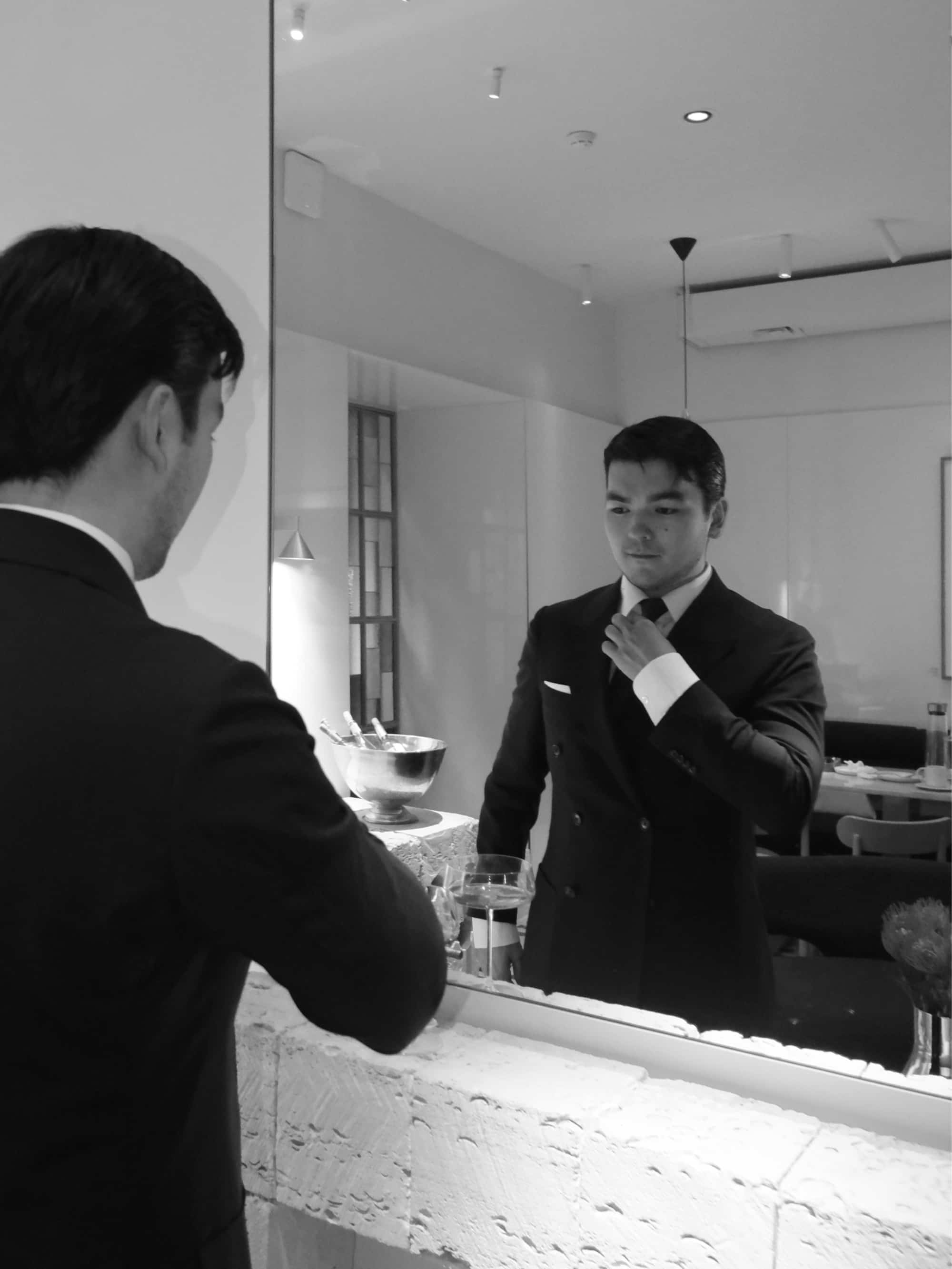 Black-and-white photograph of Almás adjusting his tie in a mirror