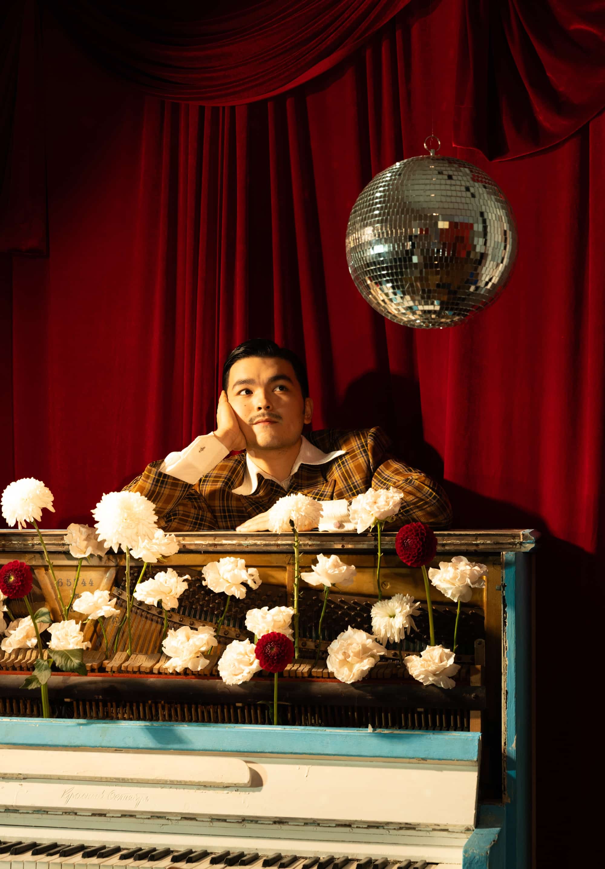 Almás resting on an open upright piano filled with white flowers, a disco ball above