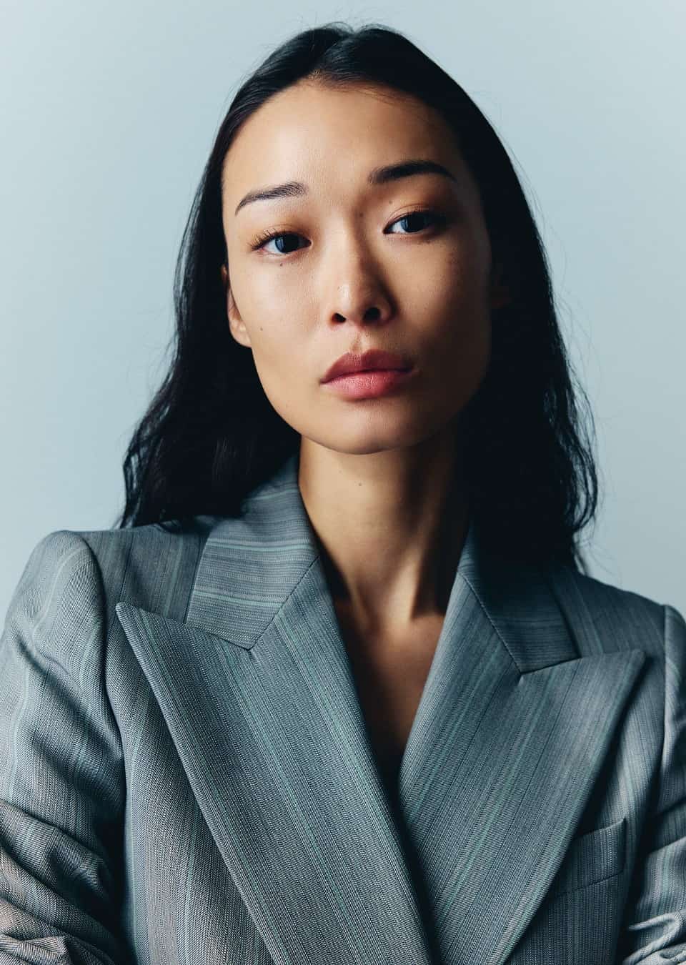 BIBI in a grey pinstripe blazer, looking directly at the camera