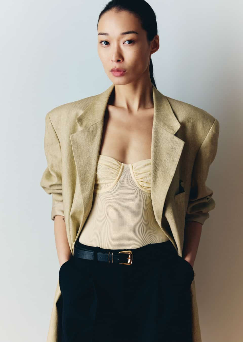 BIBI in a beige blazer and black trousers, hands in pockets