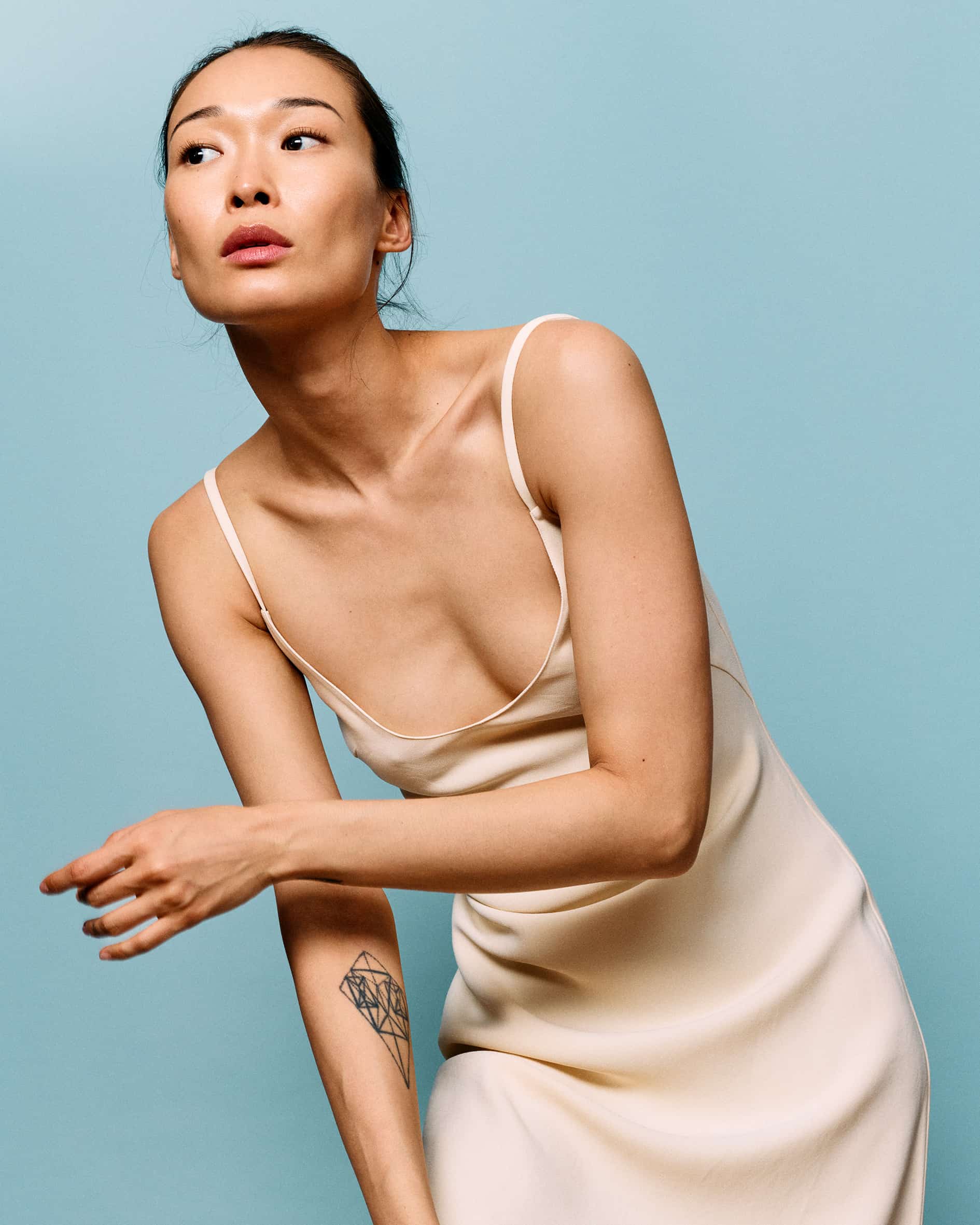 BIBI in a cream silk slip dress against a pale blue backdrop